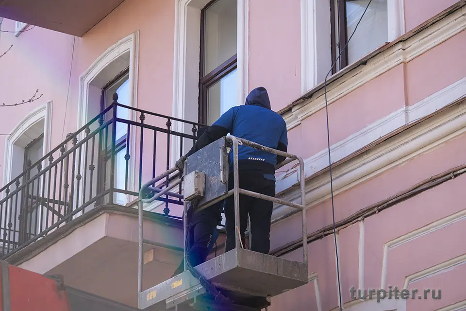 строитель поднимается на подъемнике на балкон